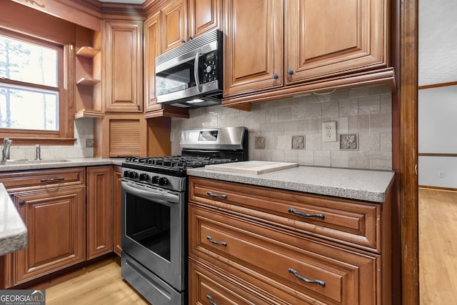 kitchen featuring stainless steel appliances, light wood finished floors, brown cabinets, and a sink