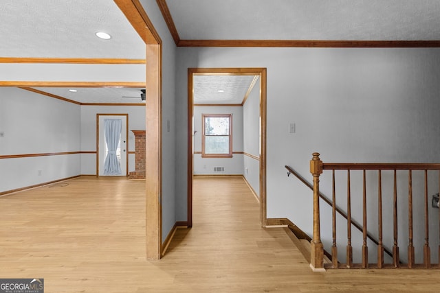 hallway featuring baseboards, ornamental molding, a textured ceiling, visible vents, and wood finished floors