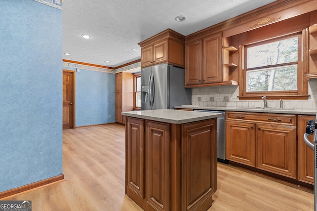 kitchen with light wood-type flooring, a kitchen island, a sink, stainless steel appliances, and brown cabinets