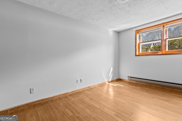unfurnished room featuring baseboard heating, a textured ceiling, wood finished floors, and baseboards