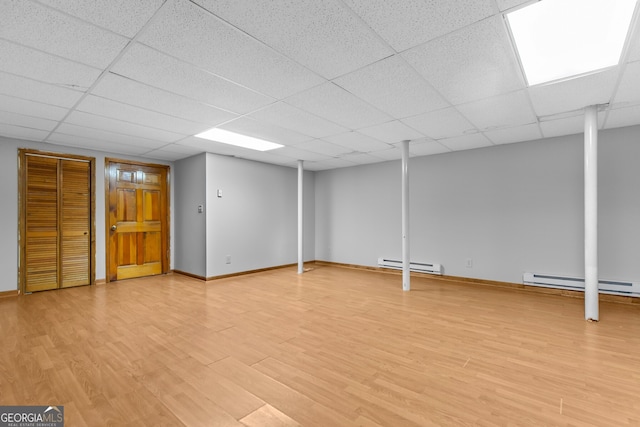 finished basement featuring a baseboard radiator, light wood finished floors, baseboards, and a drop ceiling