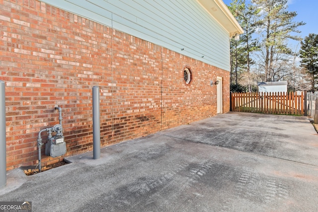 view of property exterior featuring brick siding, driveway, and fence