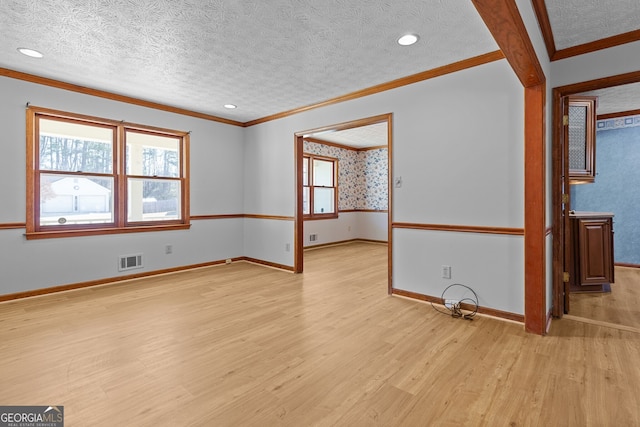 spare room with baseboards, a textured ceiling, crown molding, light wood-style floors, and visible vents