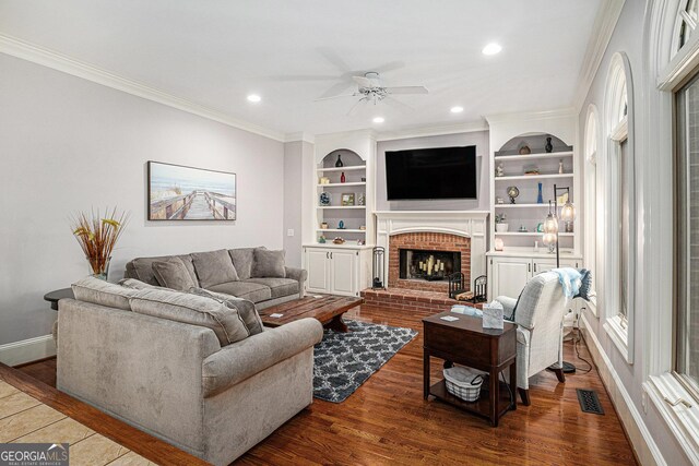 living room featuring a ceiling fan, wood finished floors, a fireplace, ornamental molding, and visible vents
