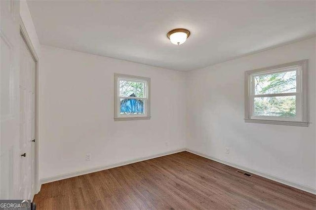 empty room with a wealth of natural light, visible vents, baseboards, and wood finished floors