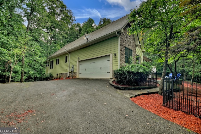 view of home's exterior featuring stone siding, a garage, fence, driveway, and roof with shingles