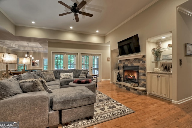 living room featuring a stone fireplace, light wood-type flooring, a ceiling fan, and crown molding