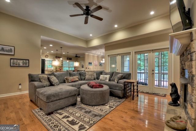 living area with wood finished floors, ceiling fan, ornamental molding, and a stone fireplace