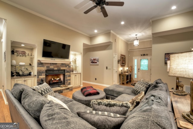 living area featuring baseboards, a stone fireplace, ornamental molding, a ceiling fan, and light wood finished floors