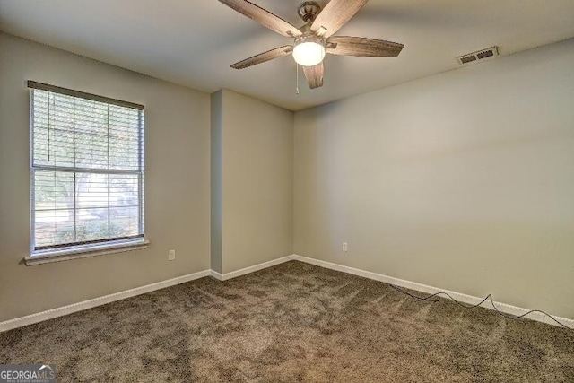 empty room with dark carpet, visible vents, ceiling fan, and baseboards