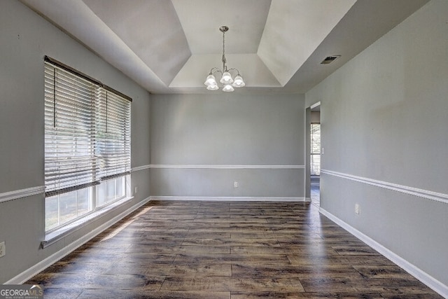 empty room featuring dark wood-type flooring, a tray ceiling, baseboards, and a chandelier