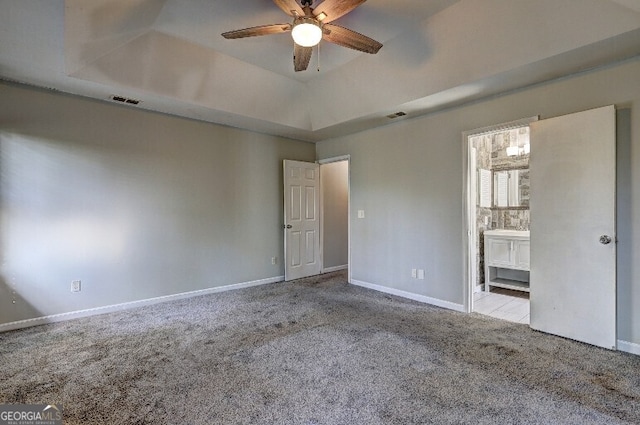interior space with a tray ceiling, carpet flooring, ceiling fan, and visible vents