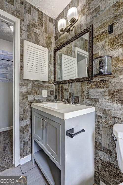 bathroom featuring a textured ceiling, vanity, toilet, wood finished floors, and baseboards