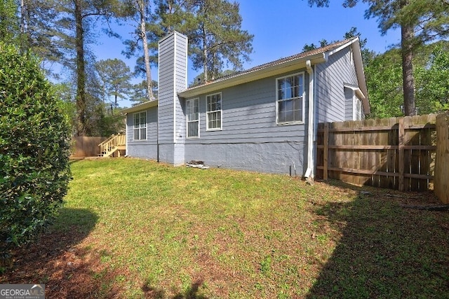 back of property featuring a chimney, fence, and a lawn