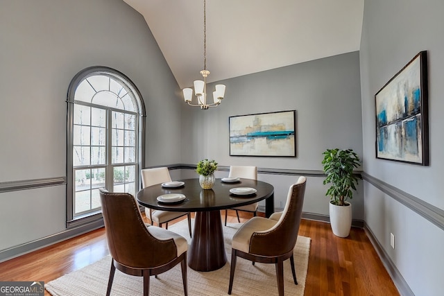 dining area with baseboards, vaulted ceiling, an inviting chandelier, and wood finished floors