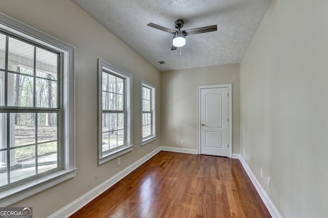 unfurnished room with a textured ceiling, wood finished floors, baseboards, and visible vents