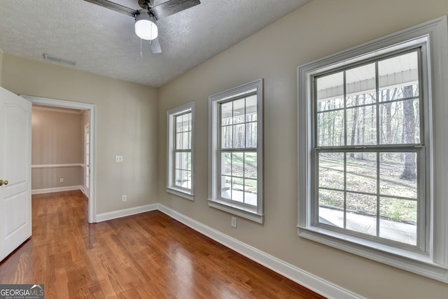empty room with baseboards, a textured ceiling, a ceiling fan, and wood finished floors
