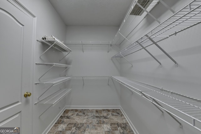 walk in closet featuring stone finish flooring