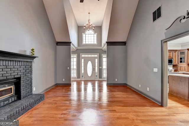 foyer featuring a notable chandelier, baseboards, a fireplace, visible vents, and light wood finished floors