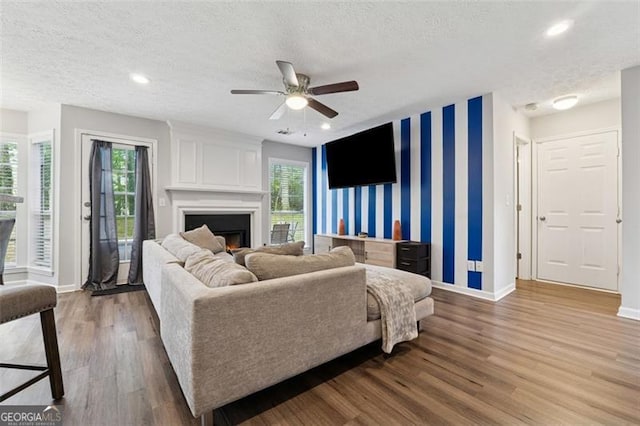living area with a textured ceiling, an accent wall, wood finished floors, wallpapered walls, and baseboards