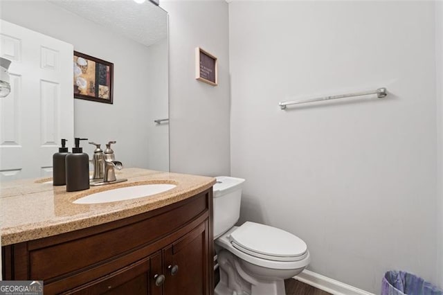 bathroom with baseboards, toilet, a textured ceiling, vanity, and wood finished floors