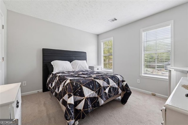 bedroom with a textured ceiling, light colored carpet, and visible vents