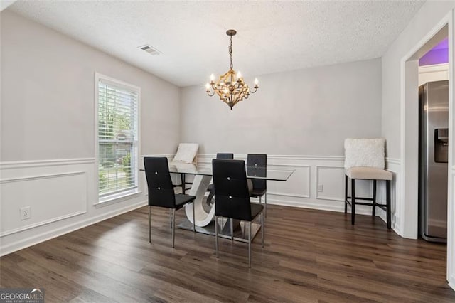 dining area featuring a notable chandelier, dark wood-type flooring, visible vents, and a textured ceiling