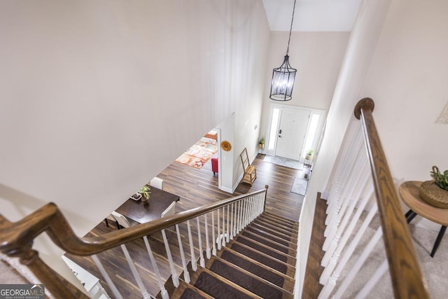 staircase with wood finished floors, an inviting chandelier, and a towering ceiling