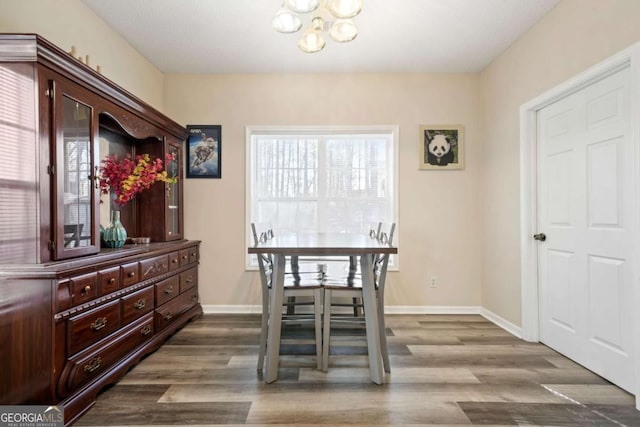 dining room with dark wood-type flooring, a notable chandelier, and baseboards