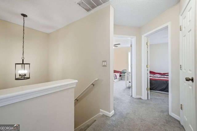 hall with a textured ceiling, visible vents, carpet flooring, an upstairs landing, and baseboards