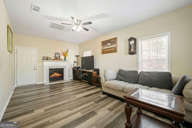 living area featuring a ceiling fan, visible vents, wood finished floors, a premium fireplace, and baseboards