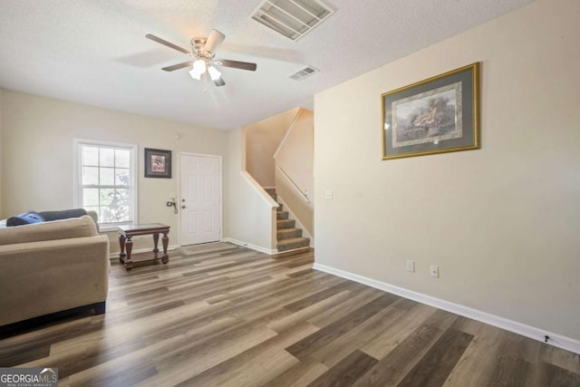 living area featuring wood finished floors, ceiling fan, visible vents, and stairs