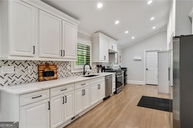 kitchen with light wood-type flooring, vaulted ceiling, white cabinets, appliances with stainless steel finishes, and a sink