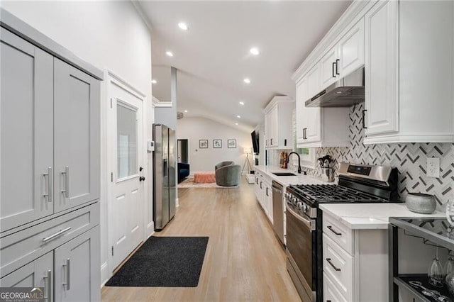 kitchen featuring vaulted ceiling, backsplash, under cabinet range hood, stainless steel appliances, and a sink