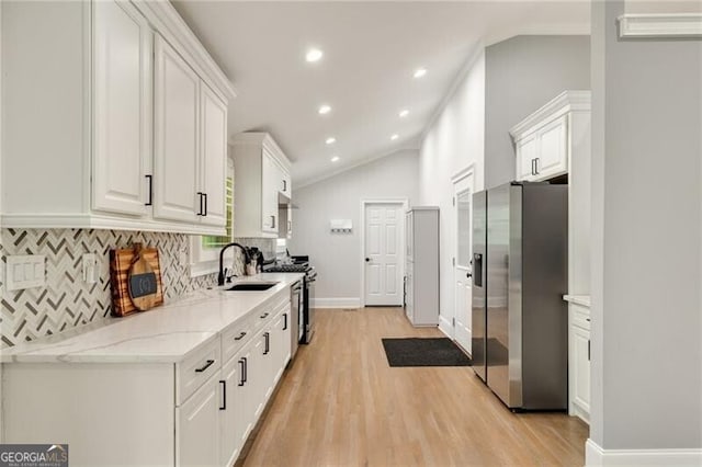 kitchen with tasteful backsplash, vaulted ceiling, white cabinets, a sink, and stainless steel appliances