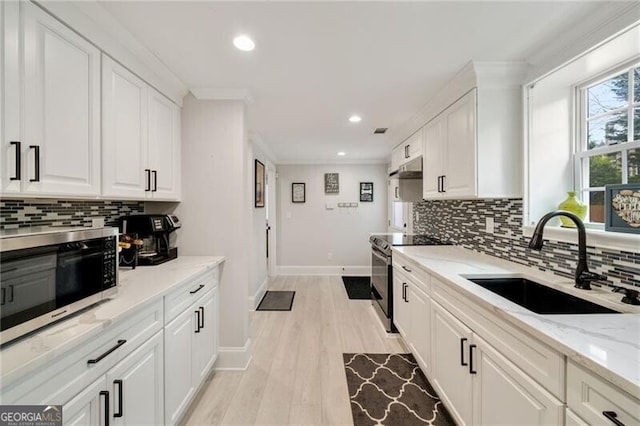 kitchen with stainless steel appliances, white cabinetry, a sink, and ornamental molding