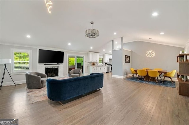 living room featuring baseboards, vaulted ceiling, a fireplace, light wood-style flooring, and crown molding