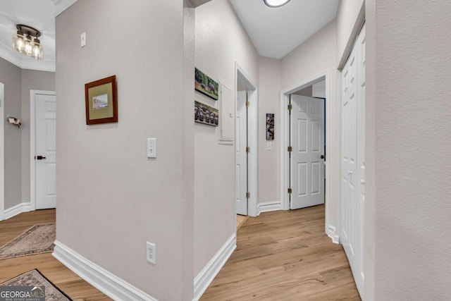 hall with light wood-style flooring, baseboards, and ornamental molding