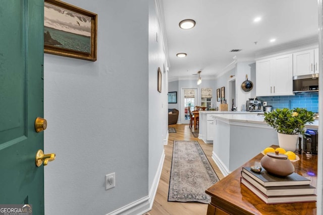 hallway with crown molding, visible vents, baseboards, and light wood-style floors