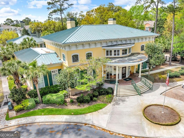 view of front of property featuring a standing seam roof, metal roof, stucco siding, and a chimney