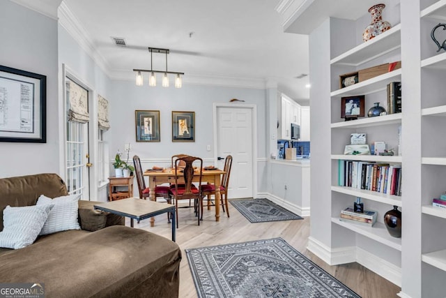 living room with built in features, visible vents, light wood-type flooring, and crown molding