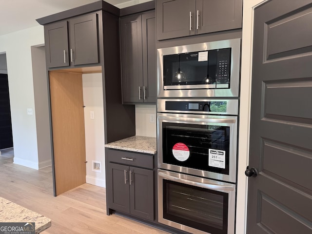 kitchen with baseboards, appliances with stainless steel finishes, light stone counters, and light wood finished floors