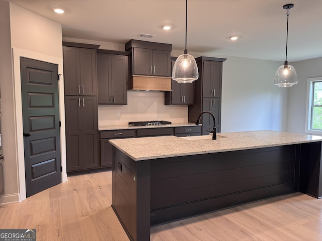 kitchen featuring light stone counters, stainless steel gas stovetop, light wood-type flooring, decorative light fixtures, and visible vents