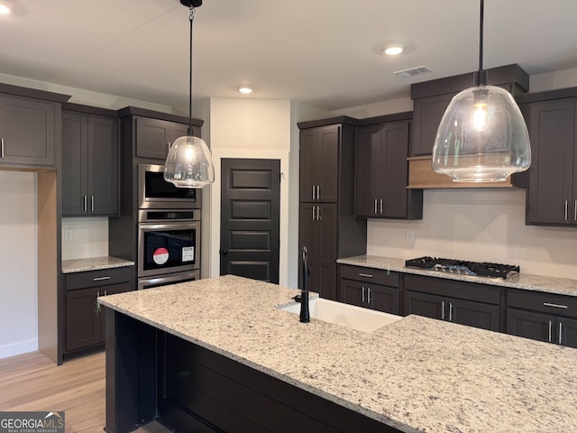 kitchen featuring visible vents, a sink, light stone countertops, light wood-style flooring, and appliances with stainless steel finishes