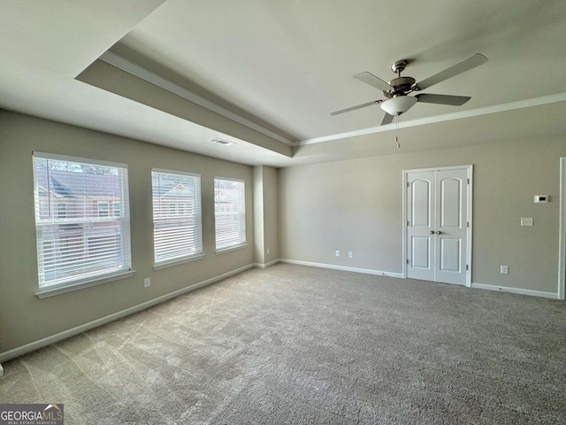 carpeted empty room with ceiling fan, baseboards, visible vents, and a raised ceiling