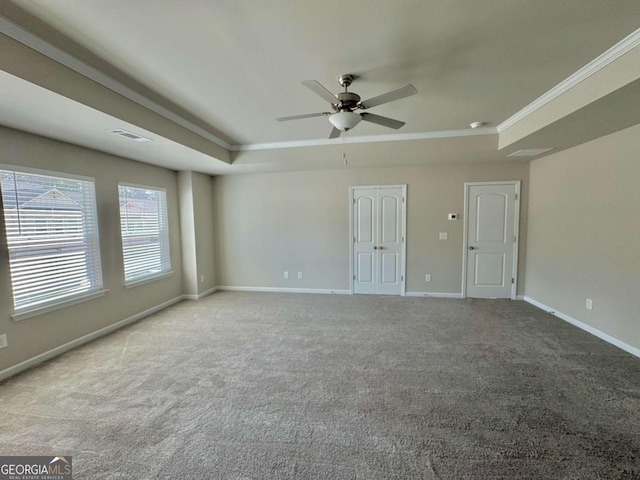 carpeted spare room featuring crown molding, a tray ceiling, a ceiling fan, visible vents, and baseboards