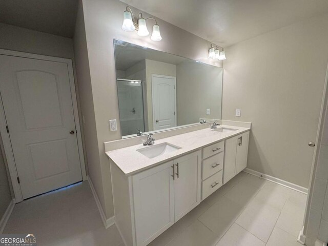 bathroom with a shower stall, double vanity, a sink, and baseboards