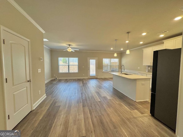 kitchen with crown molding, freestanding refrigerator, white cabinetry, light countertops, and a sink