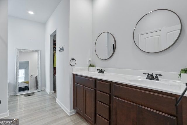 ensuite bathroom with wood finished floors, double vanity, a sink, and baseboards