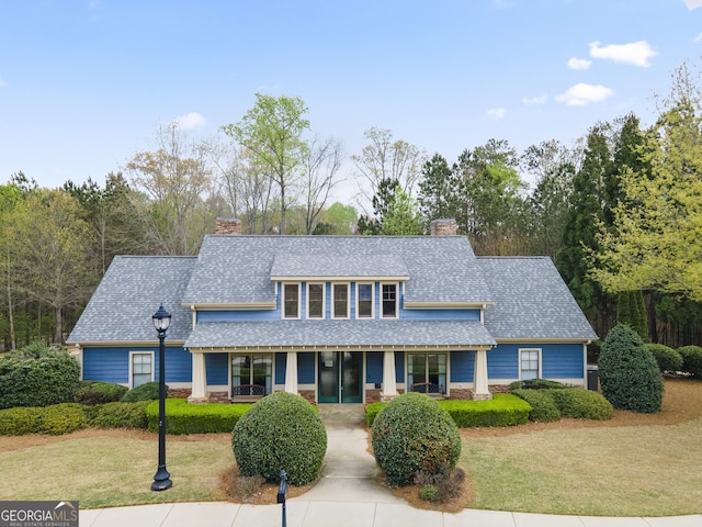 view of front of house featuring a front yard, stone siding, a chimney, and a shingled roof